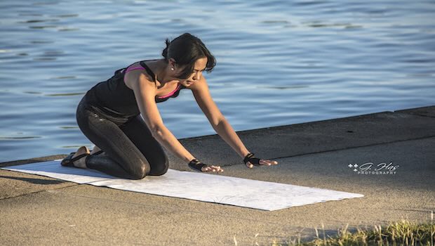 Frau macht am Ufer auf einer Matte Yoga