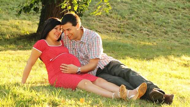 Schwangere Frau und ihr Mann sitzen auf einer Wiese